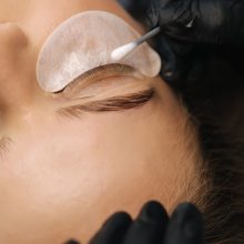 Close-up of eyelash care treatment procedures. Beautiful female, blond hair model have eyelashes lamination. Woman doing staining, curling, laminating and extension for lashes.